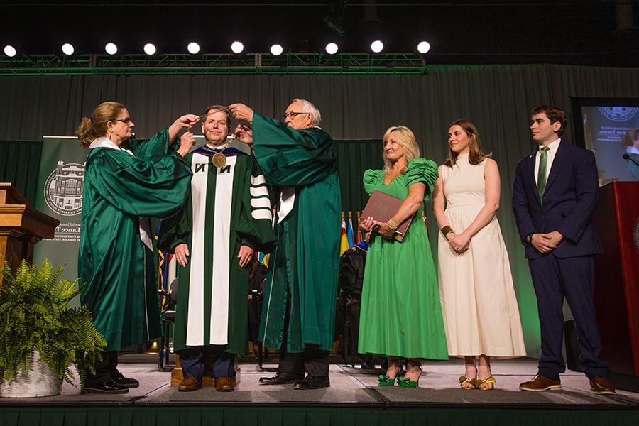 Northwest Regents Mel Tjeerdsma 和 Roxanna Swaney placed the University's chain of office on Dr. 兰斯·塔图姆的肩膀，他的家人在一旁看着. (Photo by Lauren Adams/<a href='http://ieqnui.isakichi.net'>威尼斯人在线</a>)